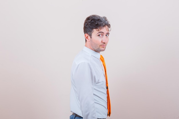 Young man looking at camera in white shirt, tie, jeans and looking confident. .