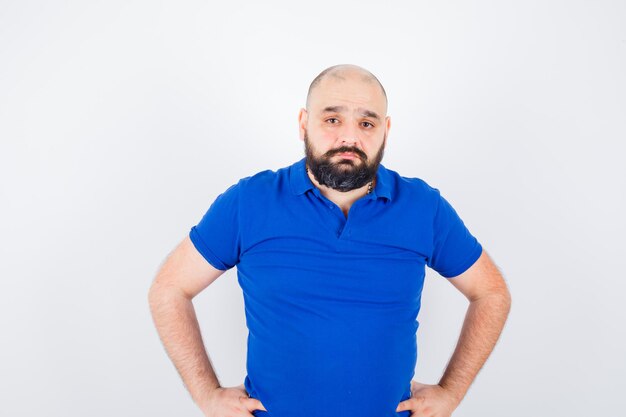 Free photo young man looking at camera with hand on waist in blue shirt , front view.