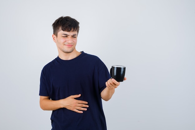 Молодой человек смотрит на чашку в черной футболке и недоволен, вид спереди.