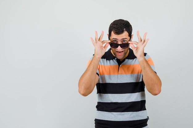 Free photo young man looking over glasses in t-shirt,sunglasses and looking pleased