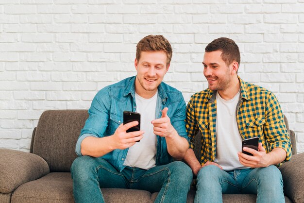 Young man looking at his friend pointing finger on smartphone