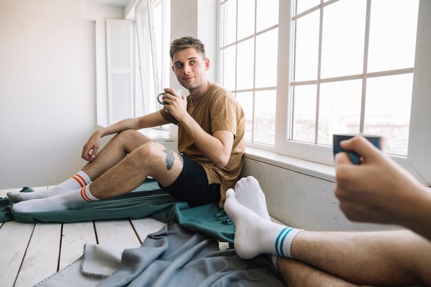 Young man looking his friend while holding coffee cup