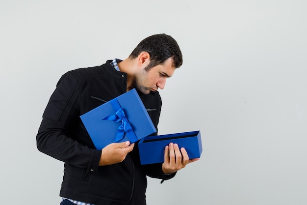 Young man looking into present box in shirt, jacket and looking curious. 