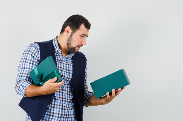 Young man looking into present box in shirt, vest and looking downcast , front view.