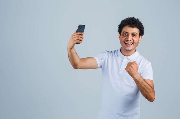 白いTシャツを着て携帯電話を見て幸せそうに見える若い男。正面図。