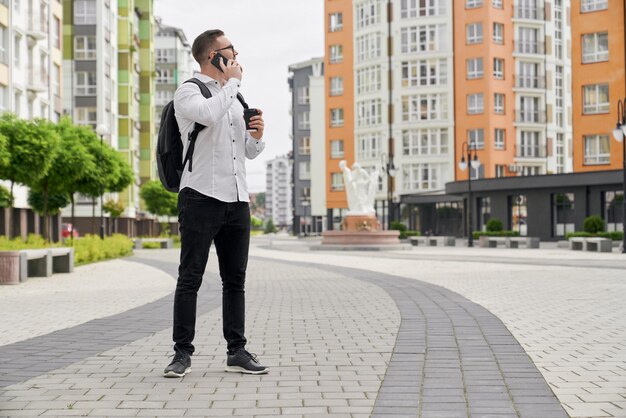 Young man looking at multistory houses talking by phone