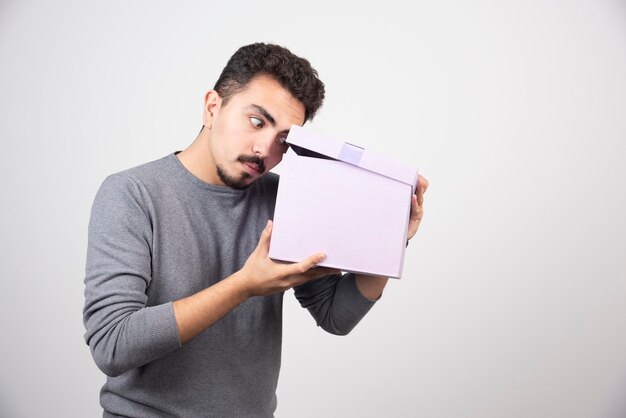 Young man looking at an opened purple box over a white wall.