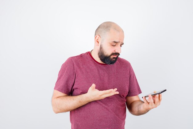 Young man looking at phone and talking someone in pink t-shirt and looking annoyed. front view.