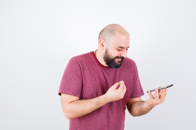 Young man looking at phone and talking someone in pink t-shirt and looking happy. front view.