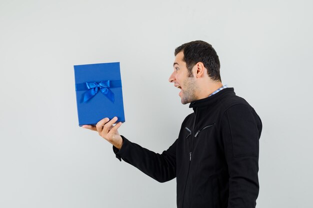 Young man looking at present box in shirt, jacket and looking joyful