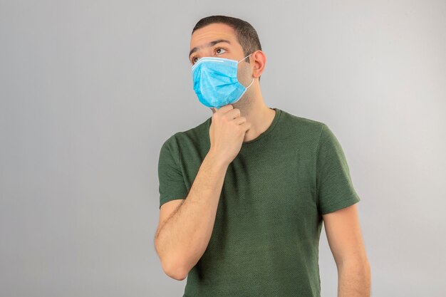 Young man looking sick wearing face medical mask holding hands on his neck because of throat pain isolated on white