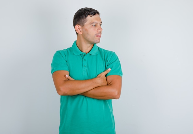 Young man looking at side with crossed arms in green t-shirt, front view.