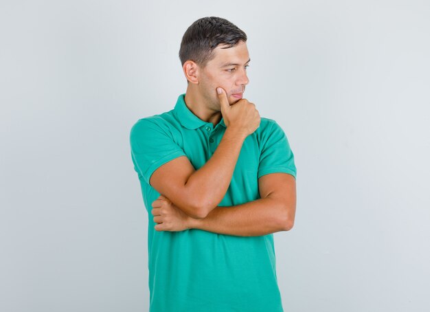 Молодой человек смотрит в сторону с рукой на подбородке в зеленой футболке и выглядит задумчивым. передний план.