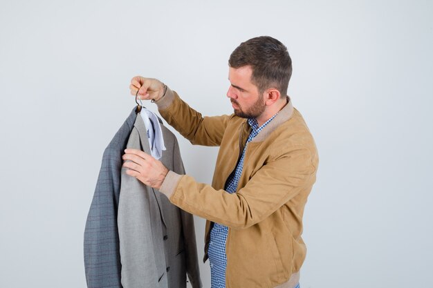 Young man looking at suits, standing sideways in jacket, shirt and looking serious.