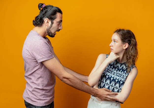 Foto gratuita il giovane guarda sorpreso dalla sua ragazza mentre lei lo guarda perplesso sul muro arancione