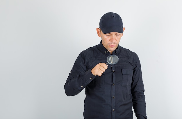 Young man looking through magnifying glass in black shirt with cap