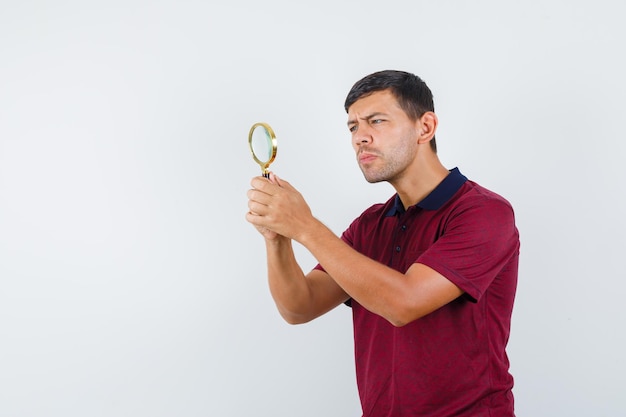 Free photo young man looking through magnifying glass in t-shirt front view.