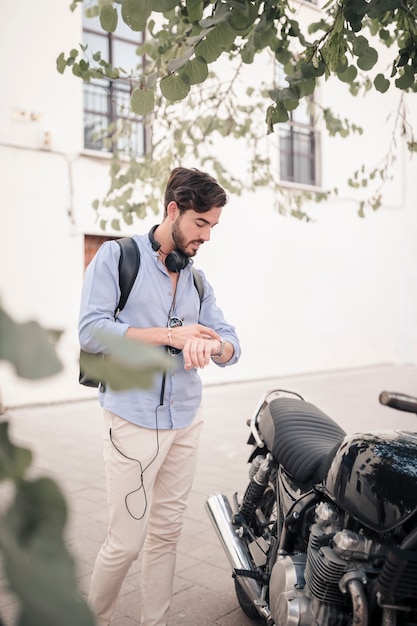 Young man looking at time on watch near his motorbike