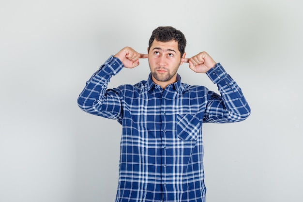 Giovane che osserva in su e che collega le orecchie con le dita in camicia controllata