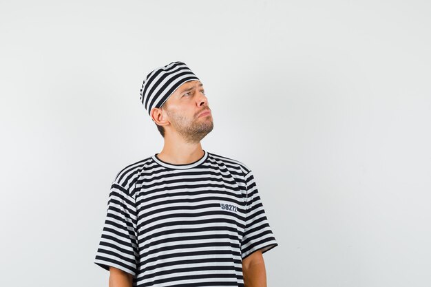 Young man looking up in striped t-shirt hat and looking thoughtful 