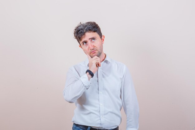 Young man looking up in white shirt, jeans and looking thoughtful