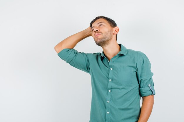 Young man looking up with hand on head in shirt and looking pensive