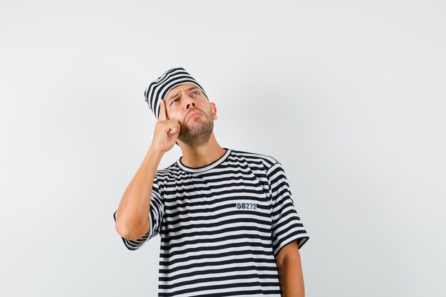 Young man looking upward in striped t-shirt hat and looking thoughtful 