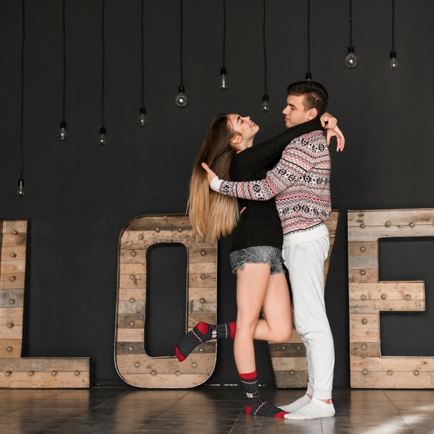 Young man loving her girl friend standing in front of wooden love text against black wall