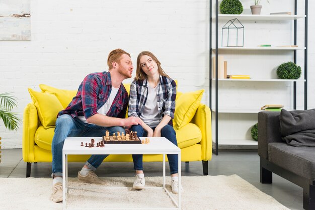 Young man loving her girlfriend sitting on the yellow sofa playing chess at home