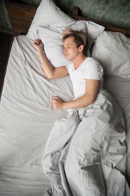 Young man lying asleep sleeping on bed alone, top view