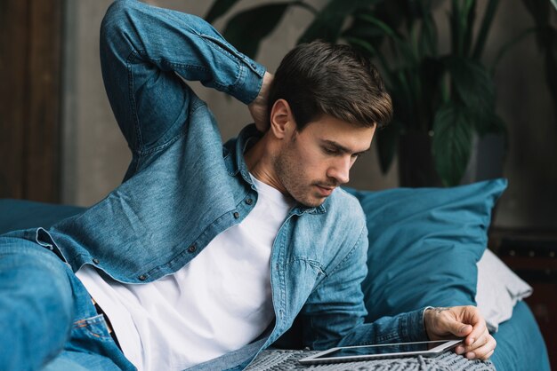 Молодой человек, лежа на кровати, глядя на цифровой планшет
