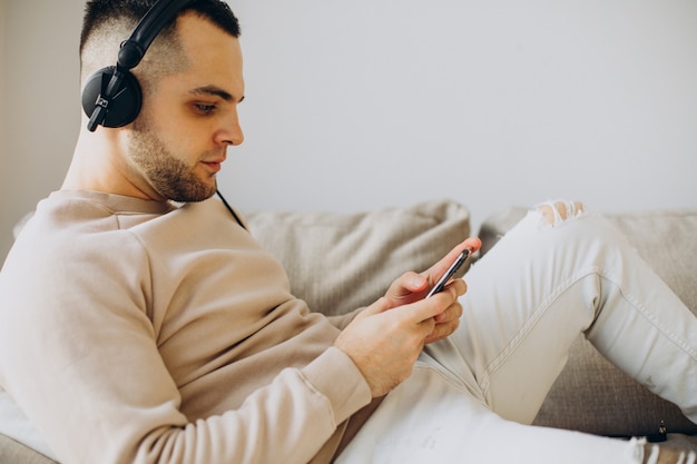 Young man lying on sofa listening to music in earphones