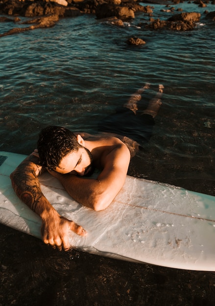 Young man lying on surf board in sea near coast 