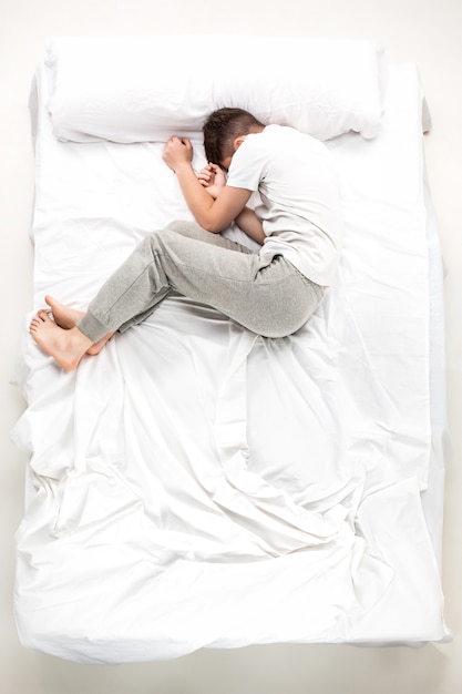 The young man lying in a white bed, top view