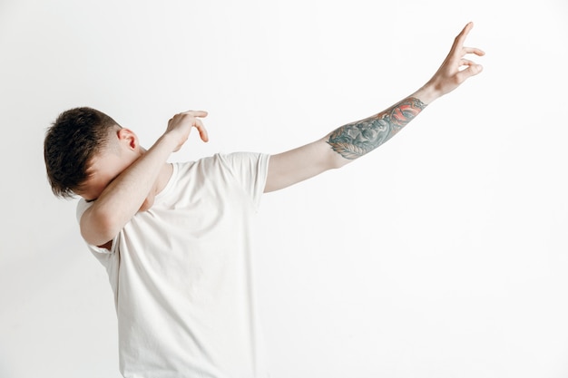 Young man makes a dab movement with his arms on a gray background. Human emotions, facial expression concept