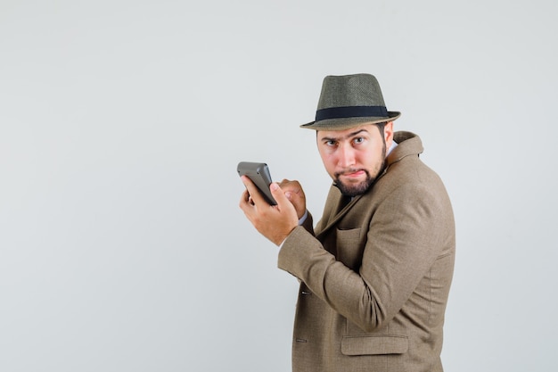 Young man making calculations on calculator in suit, hat and looking omniscient. .