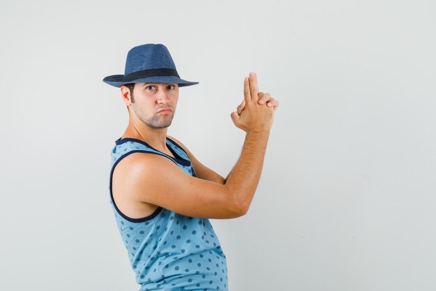 青い一重項、帽子で指ピストルサインを作って自信を持って見える若い男。