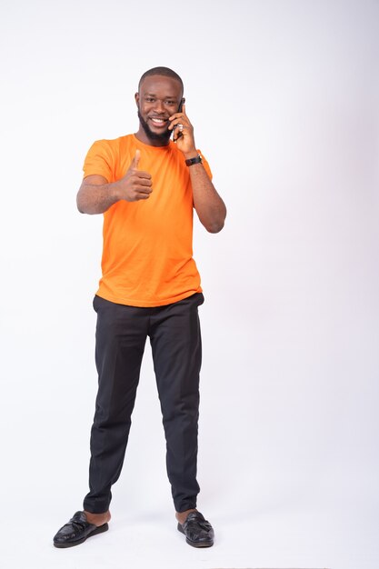 Young man making a phone call and thumbs up isolated on a white wall