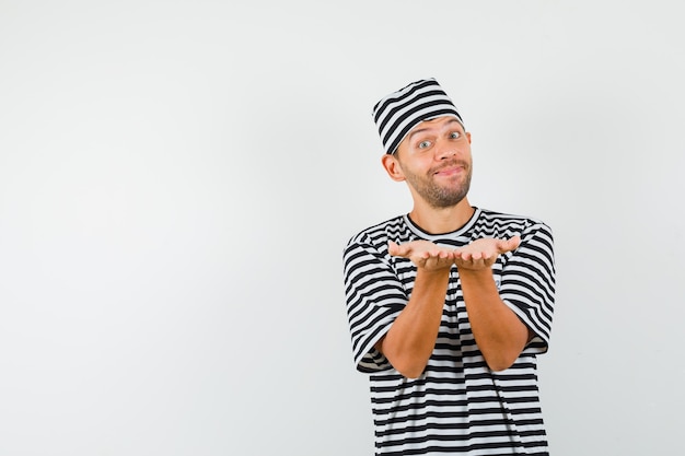 Free photo young man making receiving or giving gesture in striped t-shirt hat and looking genial