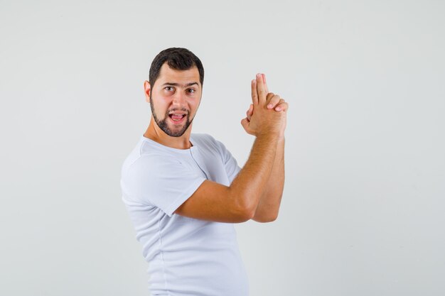 Young man making shooting gesture in t-shirt and looking brave. front view.