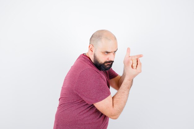 Young man making shooting gun gesture in pink t-shirt and looking brave. .