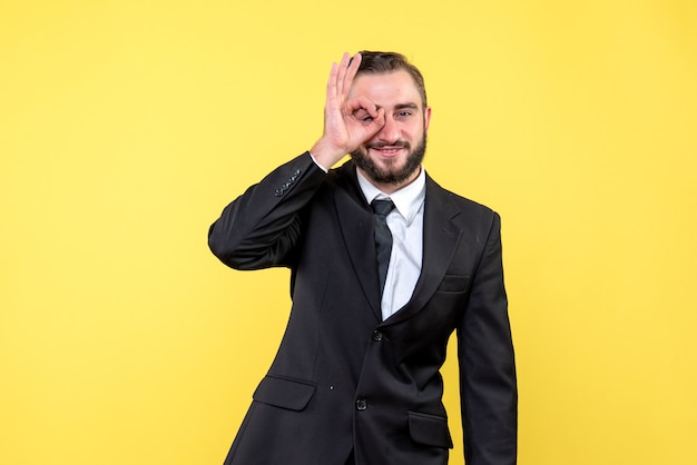 Young man making spectacle gesture while standing on yellow