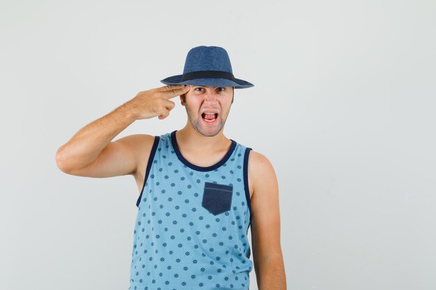 Young man making suicide gesture in blue singlet, hat and looking nervous