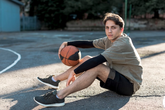 Foto gratuita uomo del giovane che si siede sul campo da pallacanestro