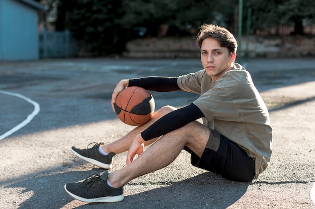 Молодой человек мужчина сидит на баскетбольной площадке
