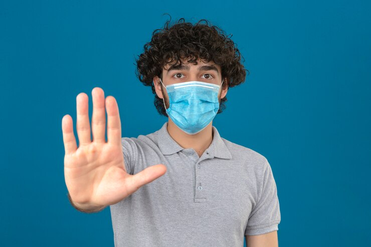 Free Photo young man in medical protective mask standing with open hand doing stop sign with serious and confident expression defense gesture over isolated blue background
