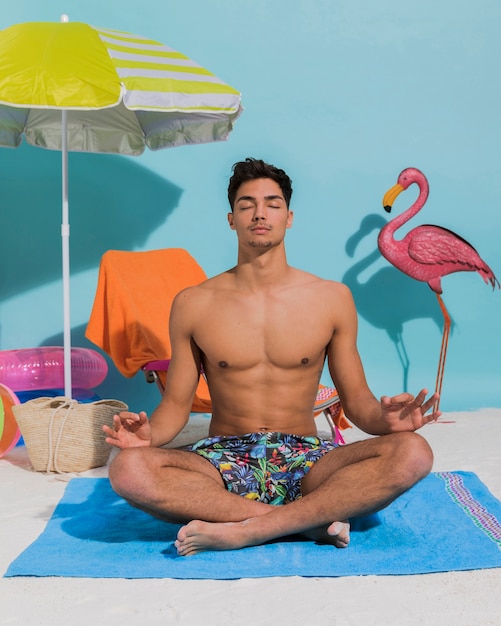 Free photo young man meditating on decorative beach