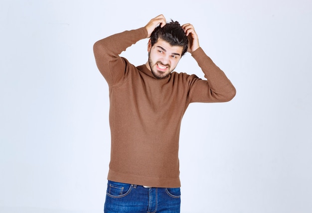 Модель молодого человека в коричневом свитере стоит и почесывает голову. Фото высокого качества