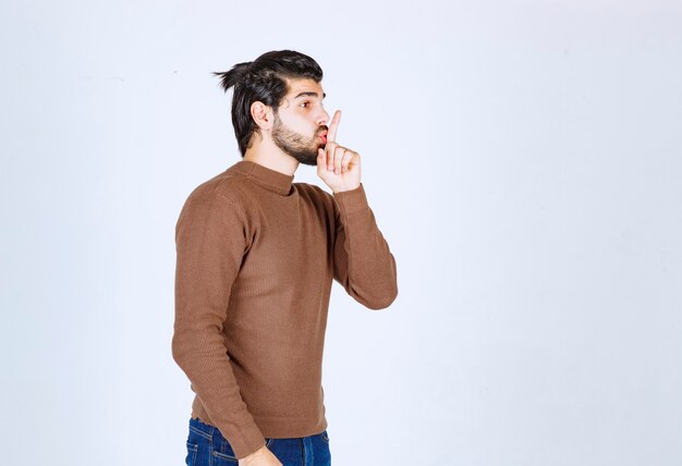 A young man model with beard standing and showing silent sign . High quality photo