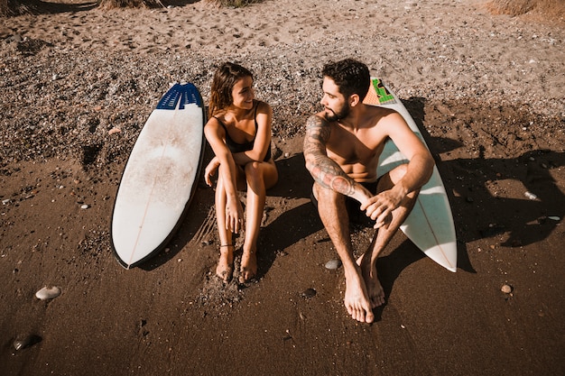 Young man near woman and surf boards on shore